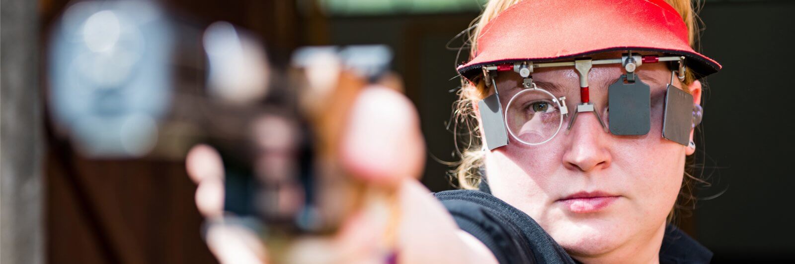 Woman aims her pistol with eye patch and visor during competition